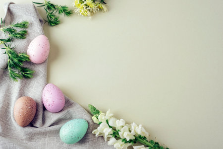 Pastel Easter eggs with flowers and green leaves on fabric on beige background. Spring flat lay copy spaceの写真素材