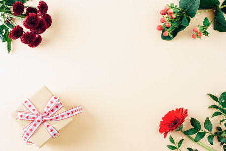 Gift box with ribbon and red flowers on beige background, festive flat lay with copy spaceの写真素材