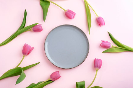 Pink tulips arranged around empty gray plate on pink background. Top view, flat lay, mockup.の写真素材