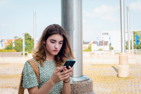 Young girl using smartphone outdoors on sunny day in modern city squareの写真素材