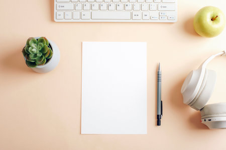Blank paper on beige desk with keyboard, cactus, headphones and pen. Home office or back to school...