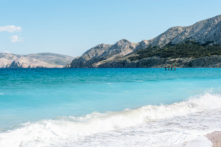 Waves gently crash on turquoise shore with rocky mountains. Baska town landscape, Krk island, Croatia. Natural backgroundの写真素材