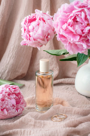 Perfume bottle and peony flowers against the background of the fabric texture