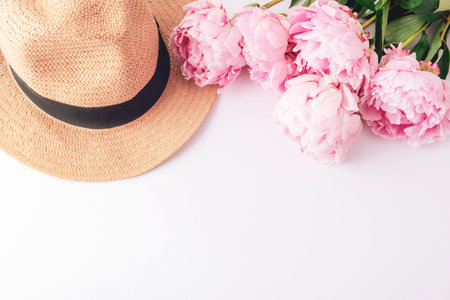 Straw hat and pink peonies arranged on white background, top view summer fashion concept. Flat lay, copy spaceの写真素材