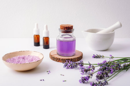 Glass bottle of lavender essential oil, sea salt, dropper bottles, mortar and fresh lavender flowers on white background. Aromatherapy conceptの写真素材