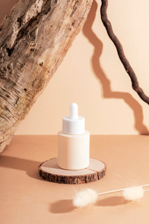 Serum bottle on wooden stand and bunny tails grass decoration on neutral beige background with sharp shadows. Natural cosmetics, skincare concept. Closeupの写真素材