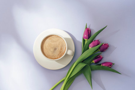 Cup of coffee with foam and purple tulips on soft lavender background in sunlight. Top view, flat layの写真素材