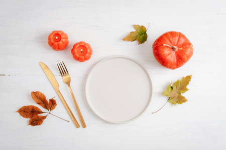 Minimal autumn table setting with plate, candles, cutlery and pumpkin on white wooden background. Top view, flat lay, mockupの写真素材