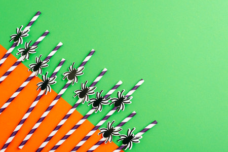 Paper straws with black spider decorations on green and orange background for Halloween party and eco friendly celebration. Top view, flat lay, copy spaceの写真素材