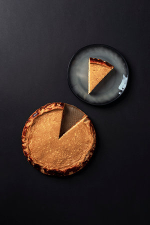 Whole cheesecake pie with one slice on black background and piece served on plate. Top view, flat layの写真素材
