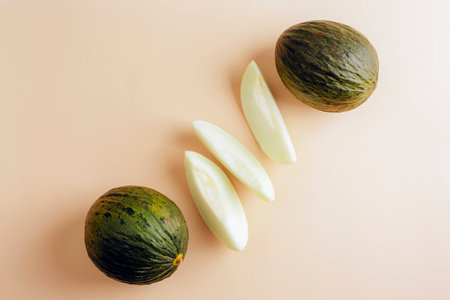 Two whole Piel de sapo melons with three slices on beige background. Top view, flat layの写真素材
