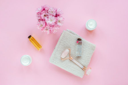Spa accessories with flowers, oils, cream and facial roller on pink background. Top view, flat layの写真素材