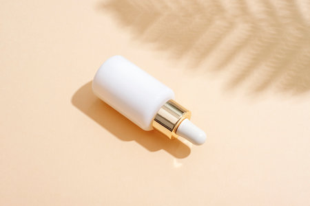 Minimalist white cosmetic dropper bottle with golden cap on beige background with fern leaf shadow. Top view, flat layの写真素材