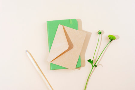 Minimalist flat lay with green notebook, kraft paper envelope, white pencil and green flower on...