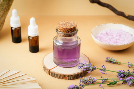 Glass jar with purple hydrolat, essential oil bottles, lavender flowers and bath salt on beige...