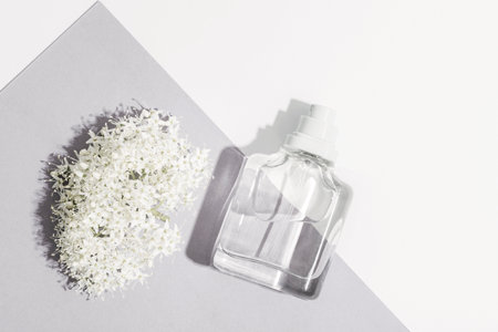 Glass perfume bottle and white blossom on white and lilac background in sunlight. Top view, flat lay. Color of the year 2026 - Cloud Dancer.の写真素材