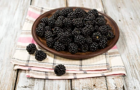 ripe blackberries in a clay bowl on a wooden backgroundの写真素材