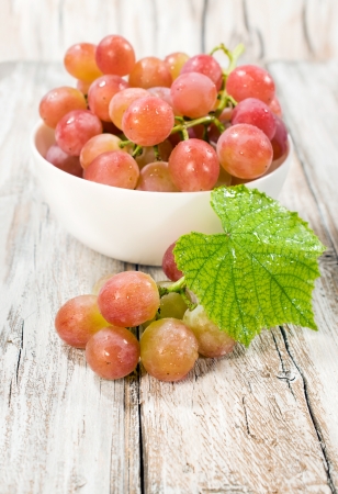 ripe grapes in a white bowl with a leaf on a wooden backgroundの写真素材