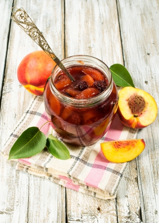 peach jam in a glass jar with fresh peachesの写真素材