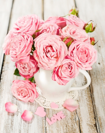 bouquet of pink roses in a vase on a painted wooden backgroundの写真素材