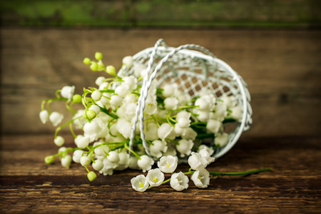 Lily of the valley in a decorative basket on wooden backgroundの写真素材