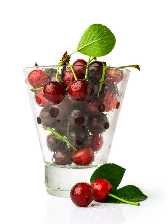 ripe cherries in glass with leaves isolated on whiteの写真素材