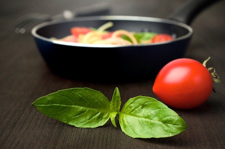 tomato with fresh basil and a frying pan with Italian pasta in the backgroundの写真素材