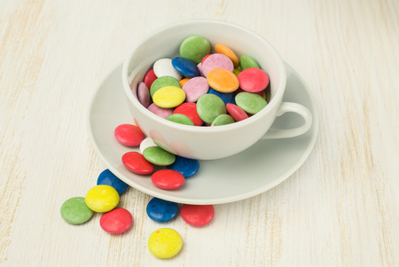 Colorful candies in a white cup on wooden tableの写真素材