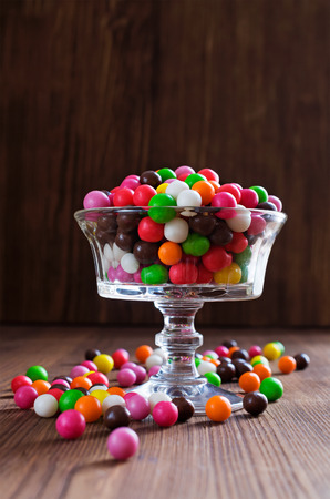Colorful round candy in a glass vase on a wooden backgroundの写真素材