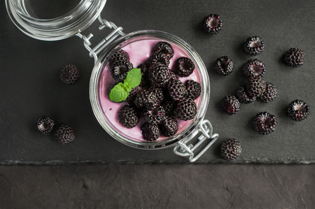 Yogurt with black raspberry or blackberry in glass jar on black slate boardの写真素材