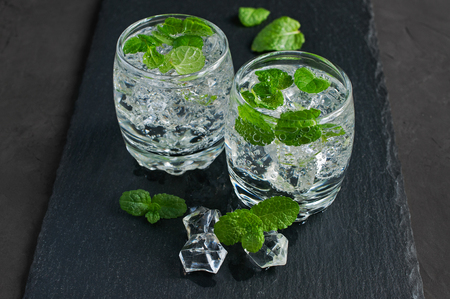 Water with ice cube and mint on a black slate boardの写真素材