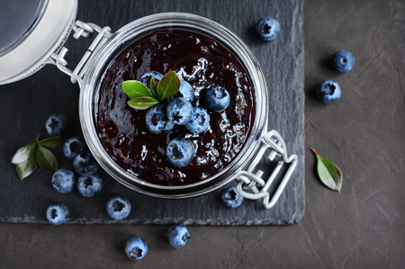 Homemade blueberry jam in a glass jar on a black slate boardの写真素材