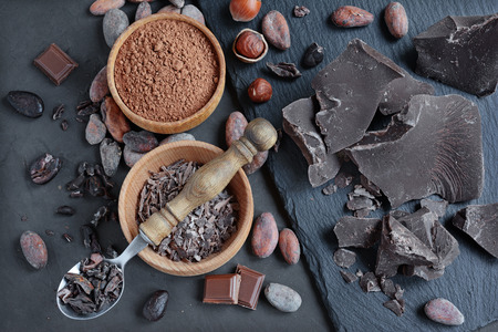 Chocolate pieces, cacao powder and cacao beans on a black slate backgroundの写真素材