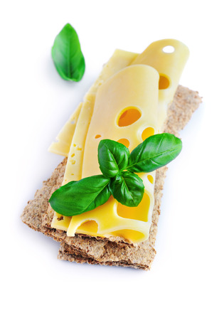 Maasdam cheese slices on crispbread with fresh basil isolated on white backgroundの写真素材