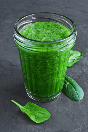 Green smoothie of fresh spinach in a glass on black slate boardの写真素材