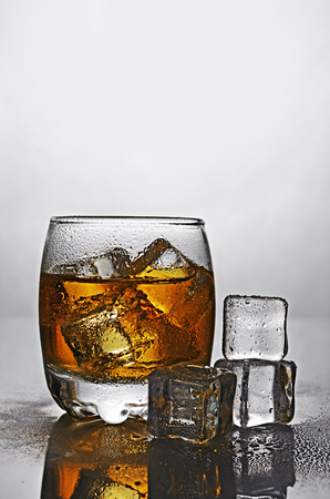 Glass of scotch whiskey with ice cube on gray gradient backgroundの写真素材