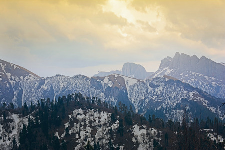 Springtime landscape of caucasus mountains covered by snow with dramatic lighting on cloudy sky backgroundの写真素材
