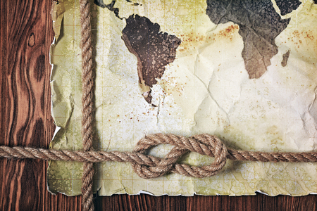 Old vintage map of the world on yellow retro stained paper with knot of rope on wood backgroundの写真素材