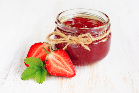 Ingredient for healthy breakfast. Homemade jam in open glass jar with fresh strawberry on bleached wood backgroundの写真素材
