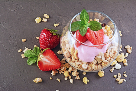 Healthy breakfast. Homemade granola and yogurt with fresh strawberry and mint in glass on black backgroundの写真素材