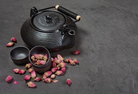 Asian black traditional teapot and teacups with dry roses for tea ceremony on dark concrete backgroundの写真素材