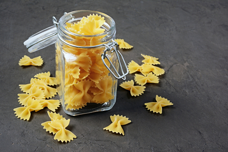 Traditional shape of dry uncooked whole wheat Italian pasta in open glass jar on black concrete backgroundの写真素材