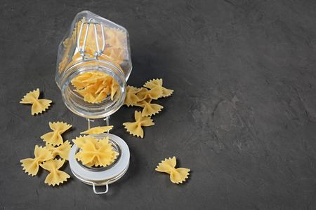 Traditional shape of dry uncooked whole wheat Italian pasta in open glass jar on black concrete...