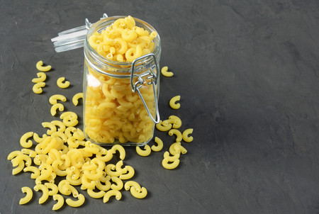 Traditional shape of dry uncooked whole wheat Italian pasta in open glass jar on black concrete backgroundの写真素材