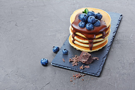 Tasty breakfast. Homemade pancakes with fresh blueberry and melted chocolate on black slate board on gray concrete backgroundの写真素材