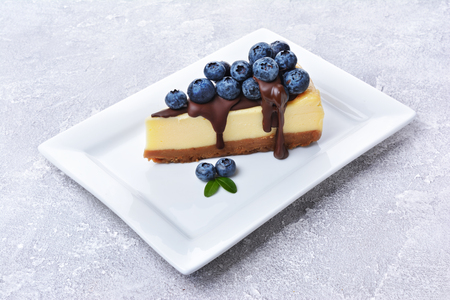 Close-up slice of delicious homemade cheesecake with fresh blueberries and chocolate cream on gray concrete backgroundの写真素材
