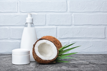 
Blank white mockup jar and dispenser bottle of cosmetic products with fresh coconut and green palm leaves on gray concrete backgroundの写真素材