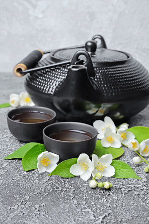 Asian black traditional teapot and teacups with healthy green jasmine tea on gray concrete backgroundの写真素材