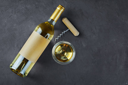 Flat lay of lying white wine bottle with empty label, corkscrew and glass for tasting on dark gray concrete backgroundの写真素材