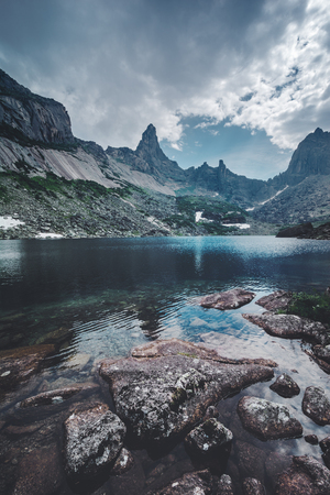 Landscape of beautiful summer picturesque mountain lake with stones and rocks on dramatic cloudy sky backgroundの写真素材